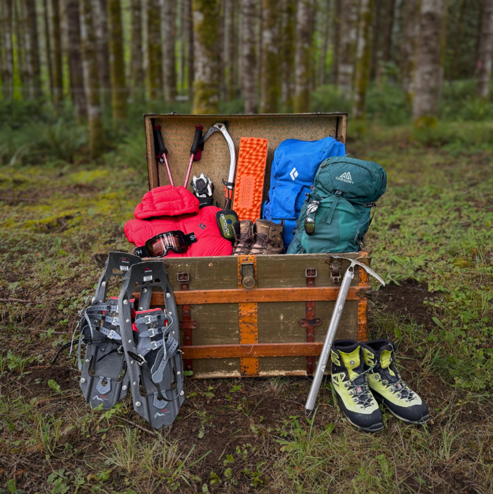 Trunk filled with outdoor gear including backpacks, shoes, and tools in a forest setting